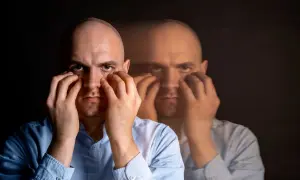 Mężczyzna z dłońmi na twarzy, z rozmazanym drugim planem sugerującym rozdwojenie.